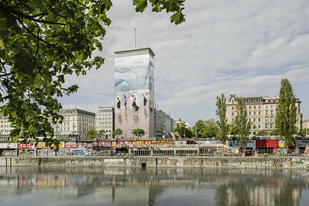 Wiener Städtische Versicherungsverein: „Wandernde Eisberge“ mitten im Wiener Stadtzentrum, Auf Initiative des Wiener Städtischen Versicherungsvereins verwandelt sich der Ringturm über die Sommermonate in eine scheinbar spielerisch sommerliche Szenerie, die Badende an einem Sandstrand zeigt. Doch die Wolken im Hintergrund und die scharfen Silhouetten, welche die slowenische Künstlerin Vanja Bućan aus dem Bild hervortreten lässt, lassen Veränderung anklingen. Credit: Wiener Städtische Versicherungsverein/Hertha Hurnaus, © Aussender (11.05.2023) 