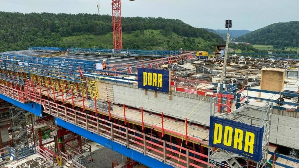 Porr: Hochbrücke Horb schiebt sich Stück für Stück übers Neckartal. Die Stahl- und Ingenieurbauteams der PORR sind in der Talmitte angelangt, in der bereits der zweite Pylonpfeiler der bis zu 90 Meter hohen Schrägseilbrücke bis zum ersten Querriegel fertiggestellt ist. Jeder Überbauabschnitt endet mit der Betonage der vorgefertigten Stahlbetonplatten, die als Grundlage für den späteren Fahrbahnaufbau dienen. © PORR
, © Aussender (06.08.2024) 